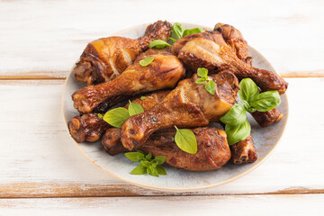 Smoked chicken legs on a ceramic plate on a white wooden background. Side view, close up.