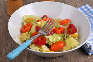 Salade composée maison avec de la iceberg et des rondelles de petits poivrons servie dans un saladier avec une fourchette