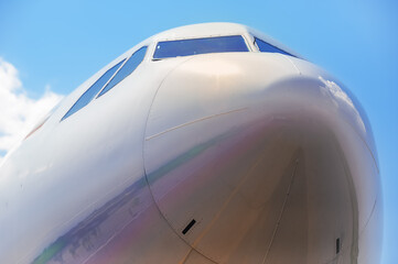 Cockpit of an airplane on a sunny day. Reflection of the runway and clouds in the body of the passenger airliner. Close view from below. No people