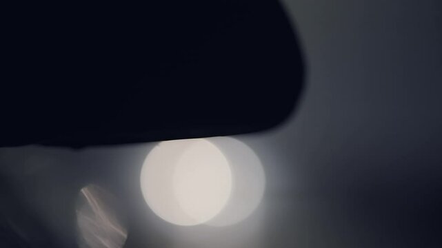Night city traffic with parked car side mirror and vehicles driving in slow motion. The image has a moody, dark atmosphere, cinematic isolated shot