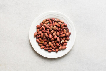 Overhead view of unpeeled raw peanuts on a white plate, flatlay of raw peanuts on a marble countertop, process of making roasted peanuts