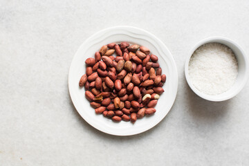 Overhead view of unpeeled raw peanuts and sugar on a marble countertop, flatlay of mise en place of ingredients for making candied peanuts, process of making candied peanuts