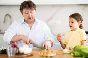 Happy father and daughter share a moment of joy in family kitchen, preparing vegetable salad