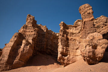 Imposing red sandstone cliffs with intricate erosion patterns against a stark blue sky in a desert...