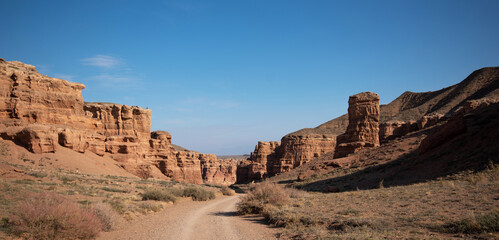 Scenic view of weathered red rock formations along a winding dirt road under a clear blue sky.