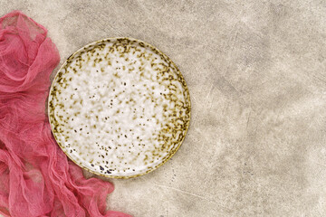 White and brown spotted plate on a pink background with red gauze above with copy space