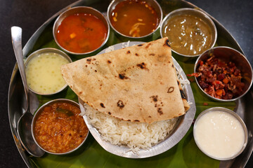 Indian vegetarian platter Thali meals. Having paneer butter masala dal makhani flat bread or naan and rice served in a steel plate and banana leaf Tamil Nadu, Bangalore Karnataka India.