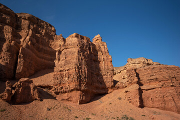 a striking formation of red sandstone cliffs set against a clear azure sky, their rugged textures highlighted by the sunlight, suggesting a peaceful desert scene in daylight