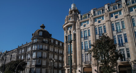 A historical building in Porto, Portugal, with intricate stonework, balconies, and an arched window, against a clear blue sky.