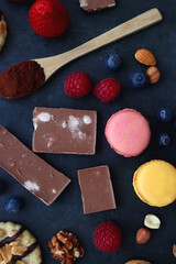 Macarons, chocolate, cookies, berries and various nuts on dark blue background. Top view.
