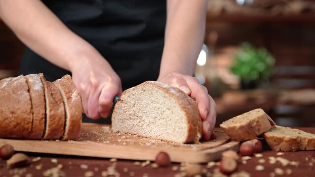 Woman in black apron slicing fresh organic bread for breakfast or dinner, closeup view of hands.