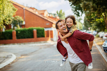 Joyful father giving piggyback ride to son on suburban street
