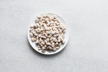 Overhead view of raw coated peanuts on a white plate, flatlay of peanuts coated in egg and flour on a marble countertop, process of making cracker nuts