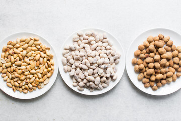 Overhead view of roasted peanuts and coated peanuts on a white plate, flatlay of roasted peeled peanuts and raw coated peanuts on a marble countertop, process of making coated nuts or cracker nuts