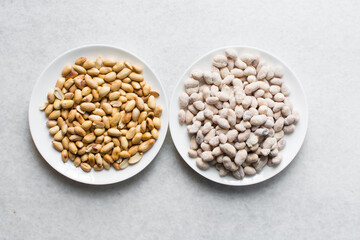 Overhead view of roasted peanuts and coated peanuts on a white plate, flatlay of roasted peeled peanuts and raw coated peanuts on a marble countertop, process of making coated nuts or cracker nuts