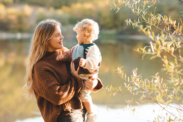 Young mother 24-26 year old holding baby over nature background. Autumn season.
