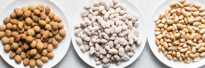 Overhead view of roasted peanuts and coated peanuts on a white plate, flatlay of roasted peeled peanuts and raw coated peanuts on a marble countertop, process of making coated nuts or cracker nuts