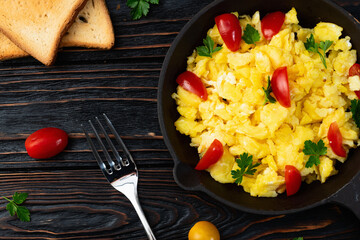 Healthy vegetarian breakfast . Scrambled eggs in pan with cherry tomatoes and parsley