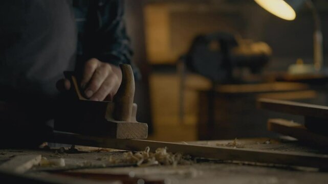 A master wood carpenter works with a block of wood using a plane to reduce the size of the wood. A woodworker uses a planer tool to work with wood his task is to give the block the desired size