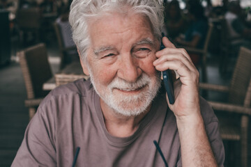 Close up portrait of senior bearded man sitting in a cafe smiling while using mobile phone. Elderly...