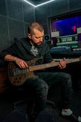 Obraz premium in the equipment of a recording room handsome man with a beard and tattoos plays an electric guitar plucks the strings choosing the right note
