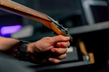 close up in the recording room equipment the sound of music handsome young guy tunes a guitar plucks the strings selecting the desired sound tonality