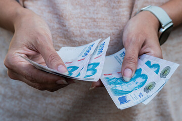 Front photo of a woman's hands counting 10,000 Argentine peso bills.