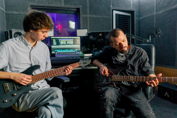 Obraz premium in the equipment of the recording room handsome man with a beard and tattoos and his young friend play the guitar in pairs and act out a song