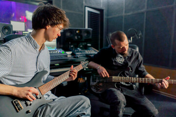 Obraz premium in the equipment of the recording room handsome man with a beard and tattoos and his young friend play the guitar in pairs and act out a song