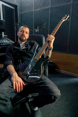 Fototapeta premium in the equipment of a recording room handsome man with a beard and tattoos sitting posing for the camera with a guitar