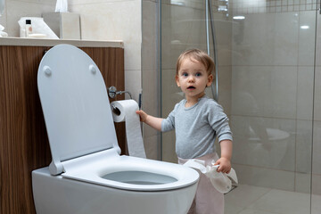 Toddler ripping up toilet paper in bathroom. Concept of naughty baby