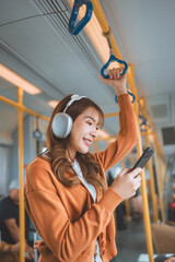 Happy young Asian woman passenger listening music via smart mobile phone in a train, Smile female wearing wireless headphones while moving in the tram, lifestyle, transportation.