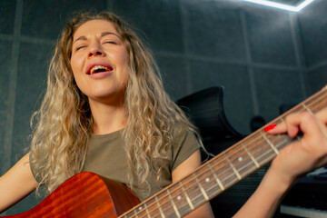 Obraz premium in the equipment of a recording room beautiful curly woman learns to play an orange acoustic guitar performing a song