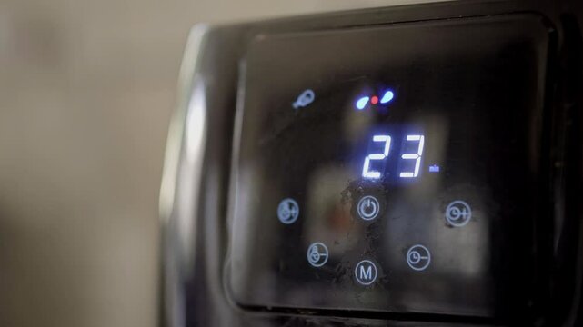 Close up of an air fryer cooking a fried chicken, the fryer's digital menu shows the cooking time and temperature.