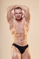 Handsome male bodybuilder posing in ab and thigh pose shirtless in briefs showing six-pack isolated...