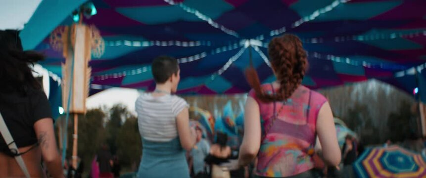 Excited female friends run toward the dance floor at an outdoor music festival. Captured using an anamorphic lens and presented in the 2.39:1 CinemaScope aspect ratio.