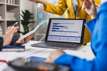 Businesswoman presenting to colleagues in conference room by standing presentation showing charts and data.