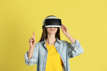 Smiling woman using virtual reality headset on yellow background