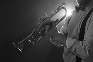 Professional musician holding trumpet on dark background, closeup with space for text. Black and...