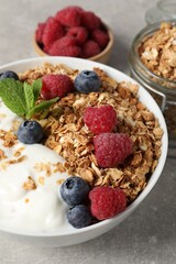Tasty granola with berries and yogurt in bowl on grey textured table, closeup