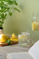 Aesthetic summer food and drink background, lemons, mint, open book, glasses and jug with lemonade iced beverage on brown wooden table, soft green backdrop