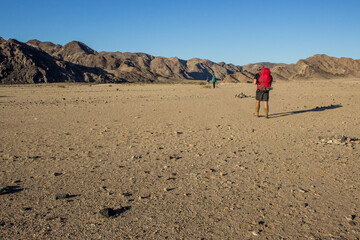 A line of hikers walking through the vast and barren windswept landscape in the lower point of Fish...