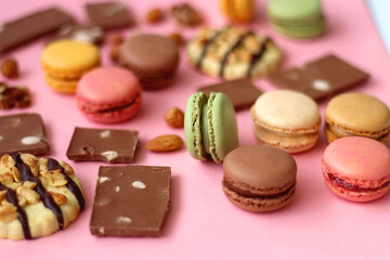 Pastel macarons, almond chocolate, peanut butter cookies and various nuts on bright pink background. Selective focus.