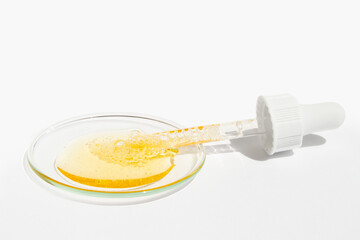 Cosmetic yellow liquid and pipette on round glass on light background