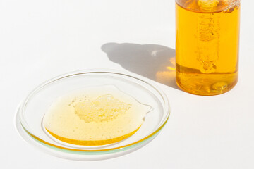 Cosmetic yellow liquid and jar on round glass on light background
