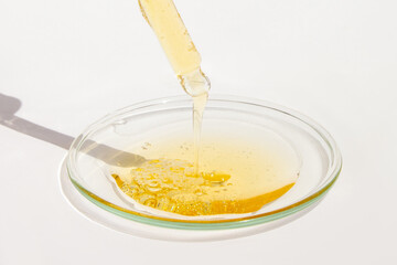 Cosmetic yellow liquid dripping from pipette on round glass on light background
