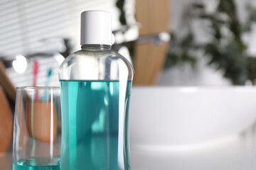 Bottle and glass of mouthwash in bathroom, closeup