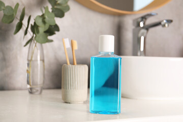 Bottle of mouthwash and toothbrushes on white countertop in bathroom