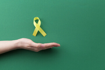 Woman with yellow awareness ribbon on green background, top view. Space for text