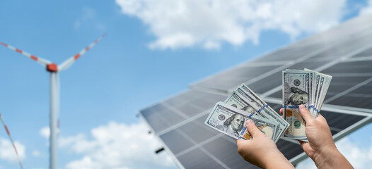 businessman holds dollars as savings after installing solar panels or wind power plants